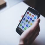 Close-up of a person holding a smartphone with various app icons visible on the screen.