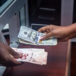 Hands exchanging US and local currency at a bank counter, signifying international finance.