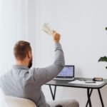 A man in a home office raises cash, symbolizing financial success and achievement.