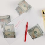 A top-down view of scattered US dollar bills with a 'past due' envelope, red pen, and notepad.