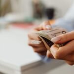 Close-up shot of hands carefully counting US dollar bills indoors at a desk.
