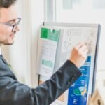 Businessman in suit writes on whiteboard displaying mortgage loan rates during a real estate meeting.