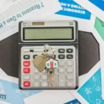 Calculator with keys and real estate documents symbolizes home buying finances.