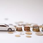 White toy sports car beside stacks of coins on a white background, emphasizing savings and finance.