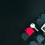 A silver key, a red house model, and a calculator on a black surface
